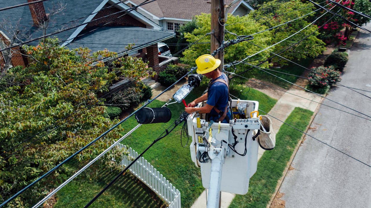 Electrician in a bucket lift repairing power lines from a utility pole in a suburban neighborhood.